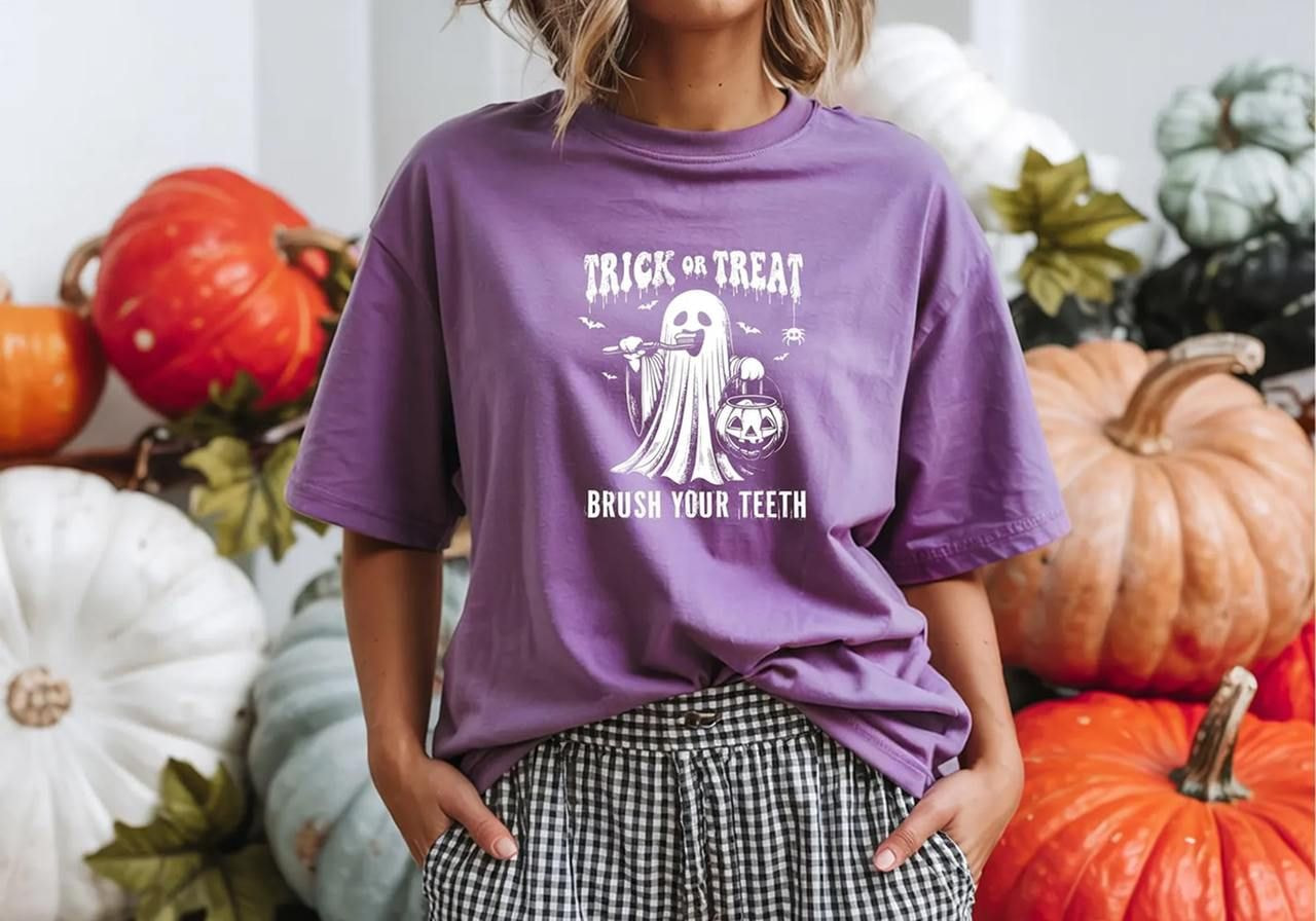 A woman in a purple t-shirt with a ghost graphic and the text "Trick or Treat, Brush Your Teeth”.